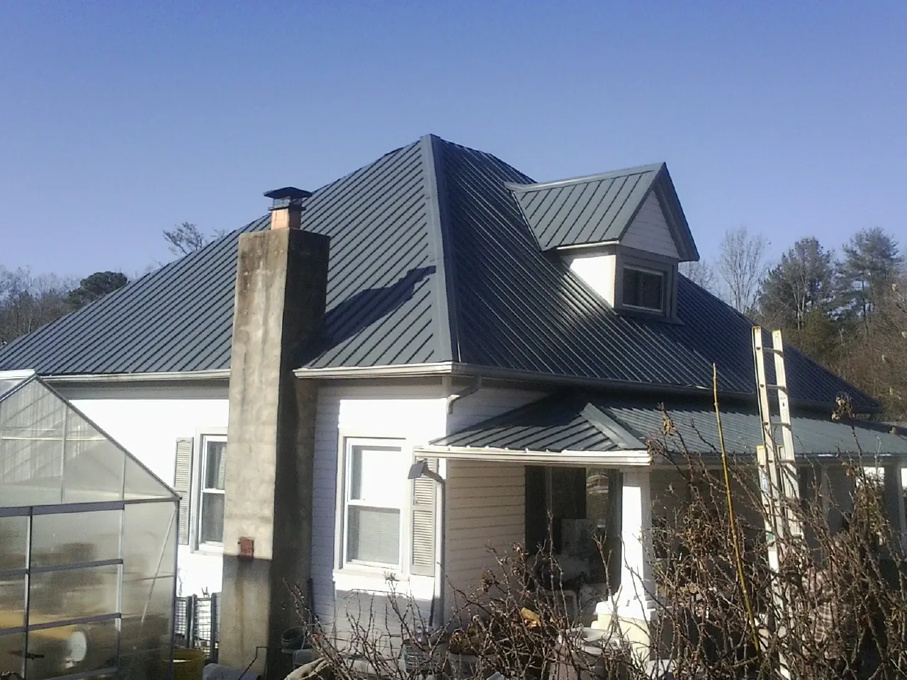 Dark blue standing seam metal roof on a white farmhouse with dormer — Slate & Tile Roof Repair by Roofing Brothers in Etters