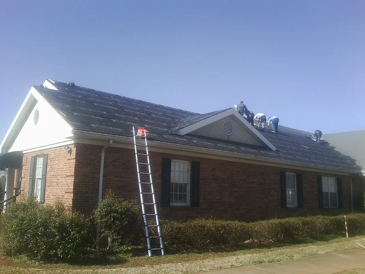 Crew tearing shingles off a brick ranch roof with a ladder set — Emergency Roof Repair work by our crew in Etters
