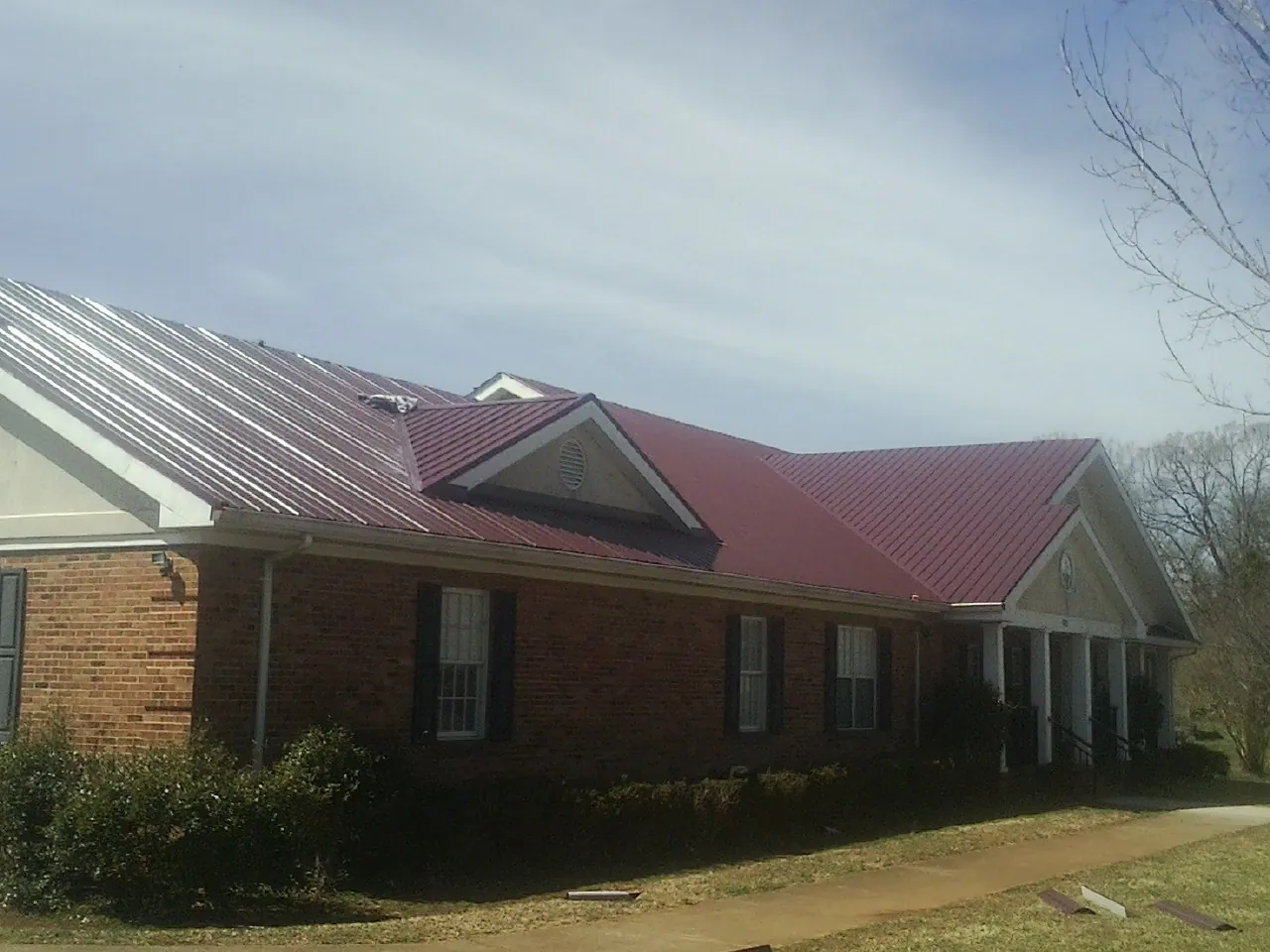 Red metal roof with gabled entries on a long brick building, from a Hail Damage Roof Repair job in Etters