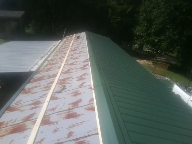 Old rusted panels beside newly installed green metal roofing — Wind Damage Roof Repair by Roofing Brothers in Etters