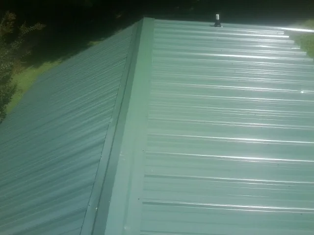 New green metal panels meeting at the ridge of a roof — Flat Roof Repair work by our crew in Etters