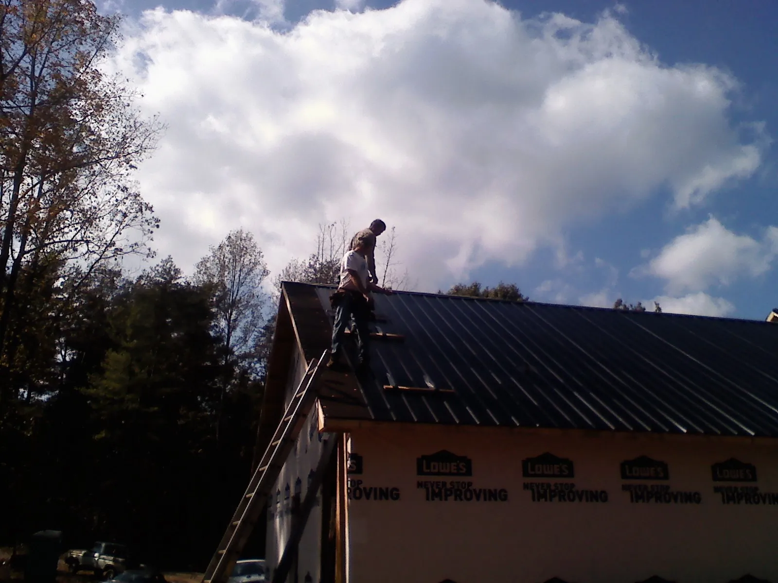 Roofer fastening dark metal panels high against a cloudy sky, from a Roof Inspection job in Etters