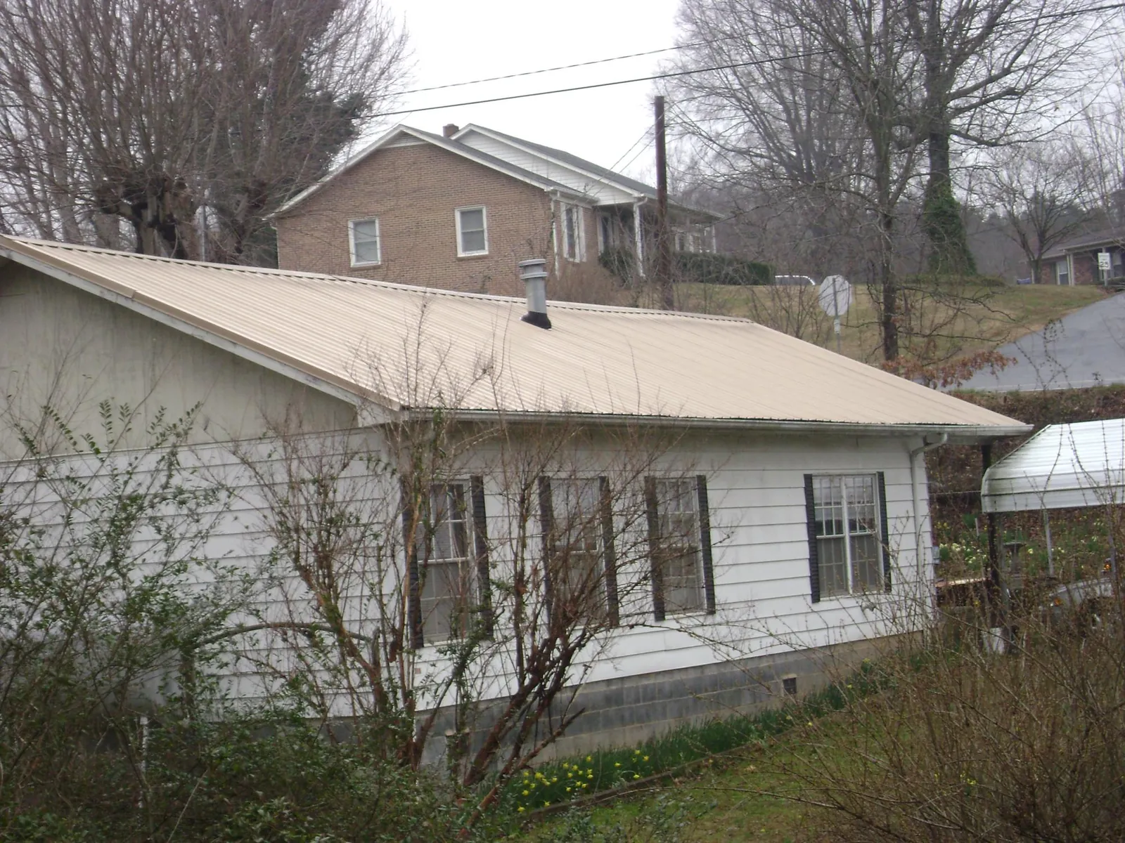 Tan metal roof on a white sided house set into a hillside — Commercial Roofing by Roofing Brothers in Etters